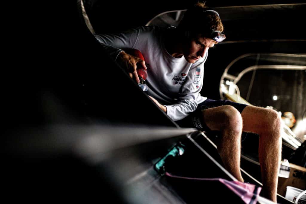 A man inside the dark hull of an America's Cup 75 inspecting the interior hull skin.