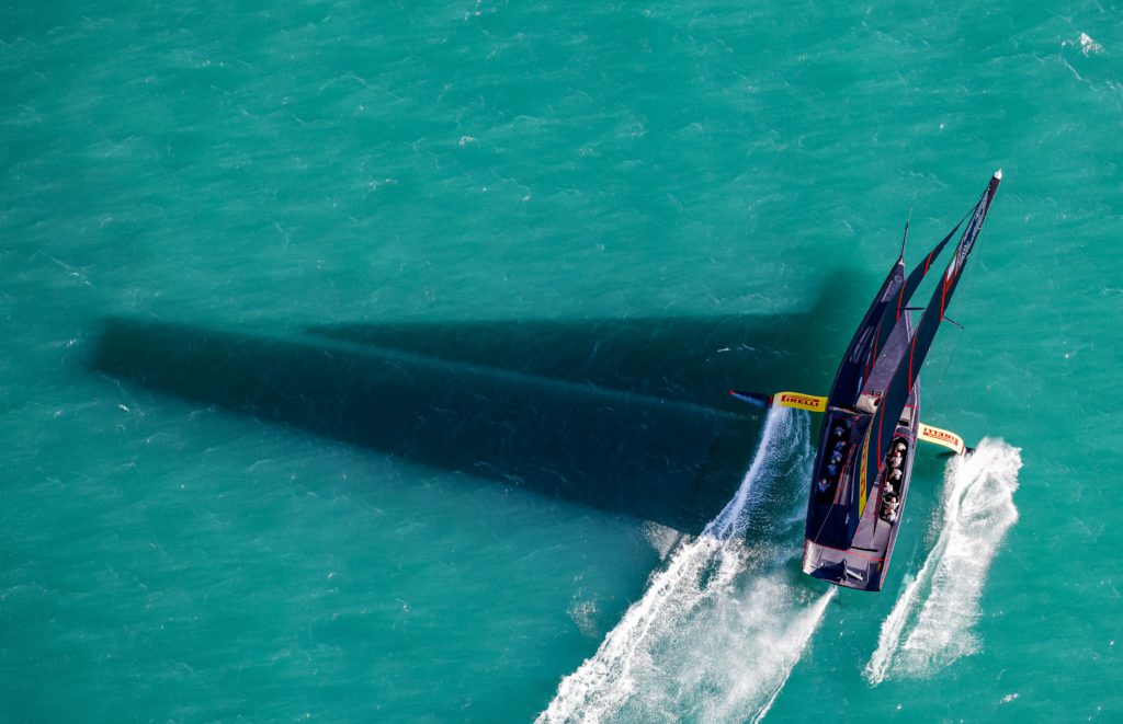 AC75 from above on blue water with sail shadow