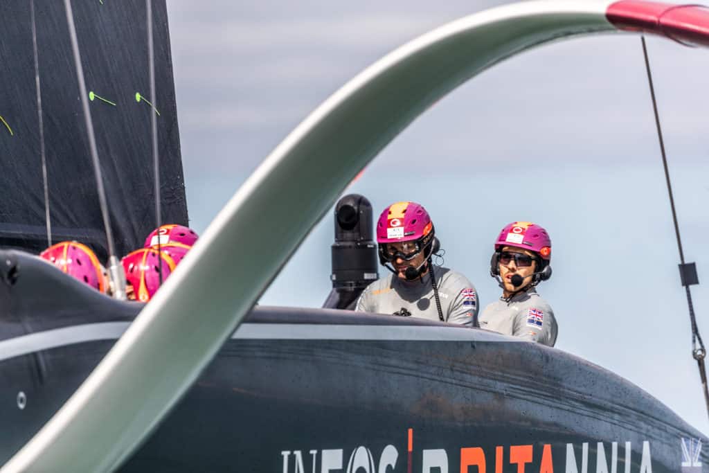 Two sailors wearing helmets on the America's Cup class 75-foot sailboat.
