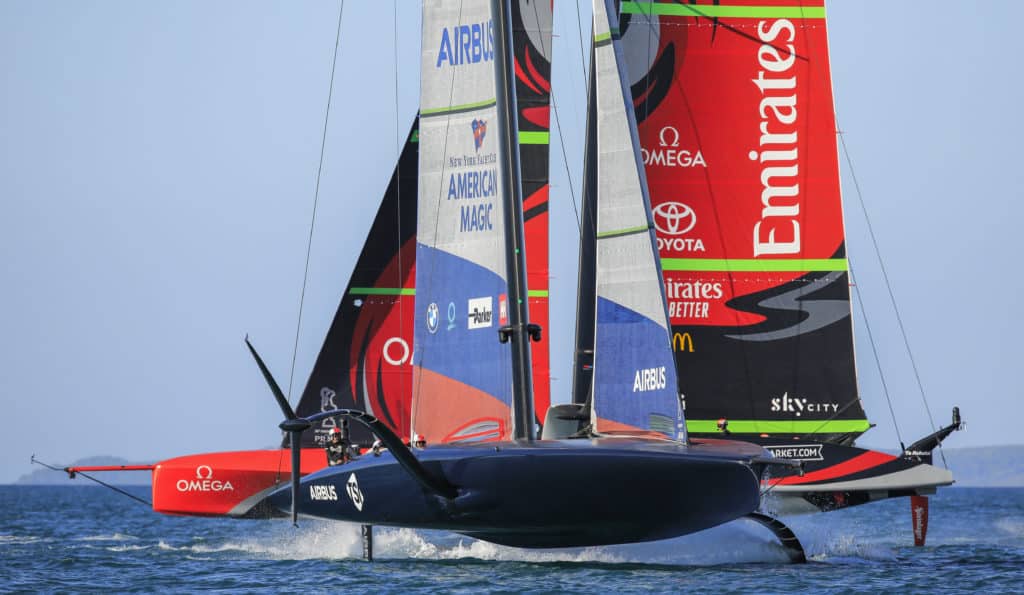 AC75s practice racing in Auckland with the American Magic team crossing Emirates Team New Zealand; both boats up on foils.