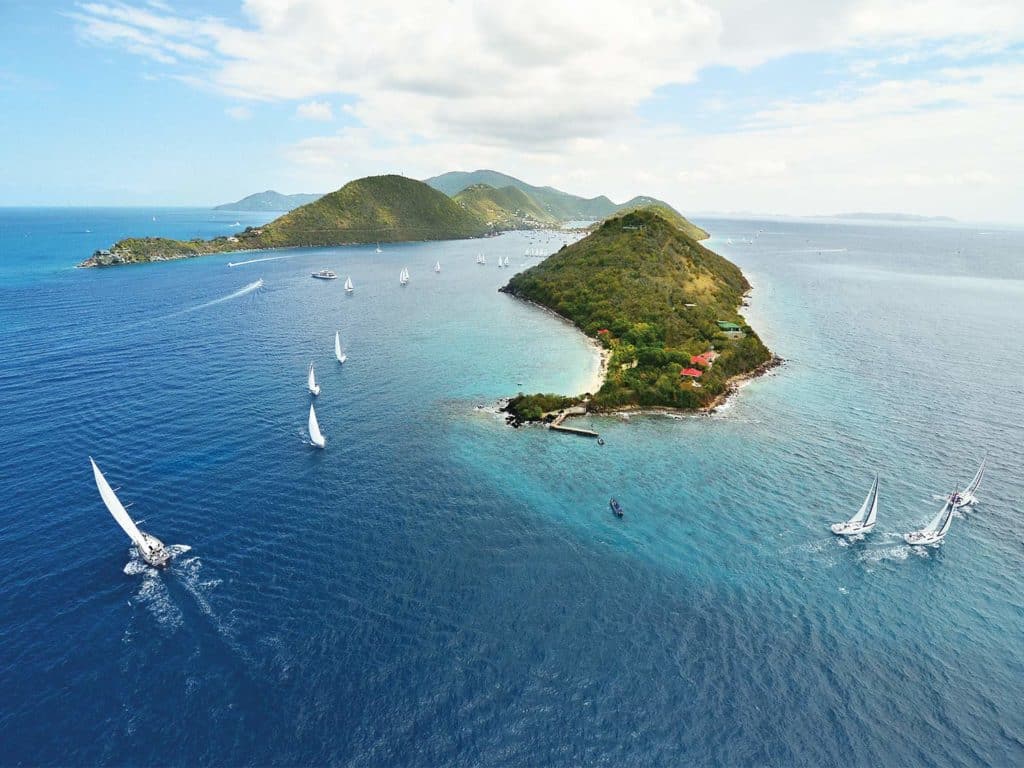 An aerial view of sailboats sailing past an island.