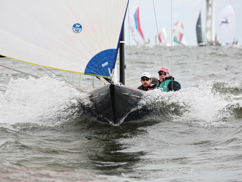 Two sailors racing a sailboat through waters, and making waves.