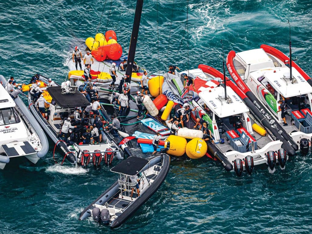 rescue boats and workers stand near a capsized sailboat.