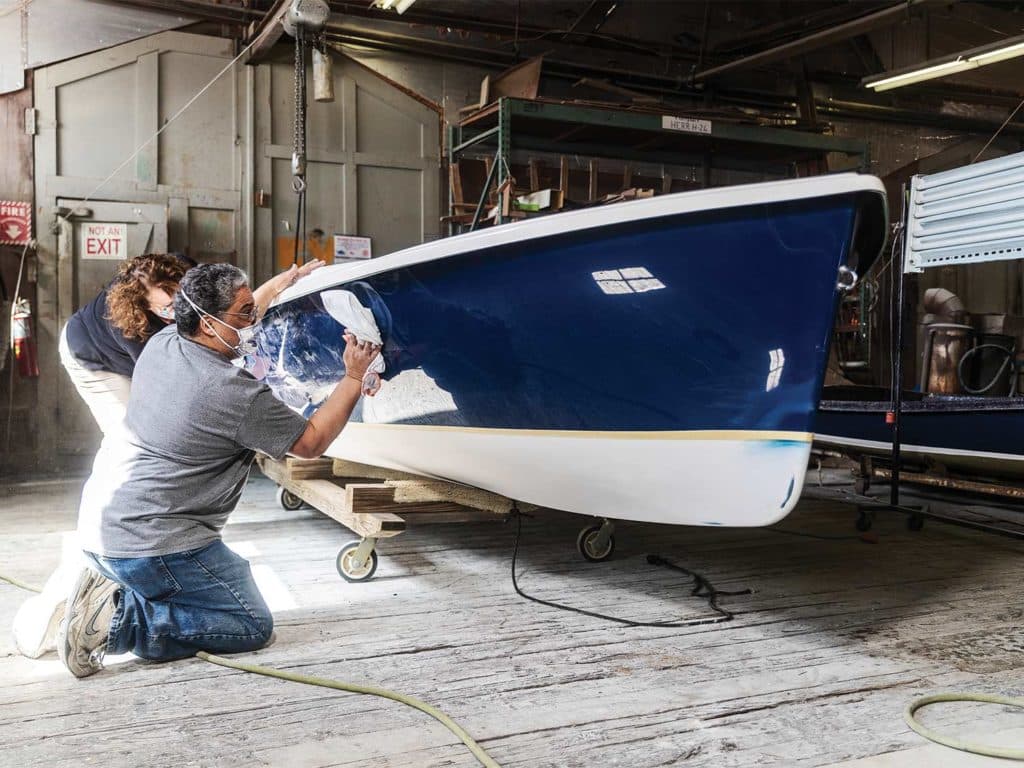 A man and a woman polish a hull of a sailing boat.