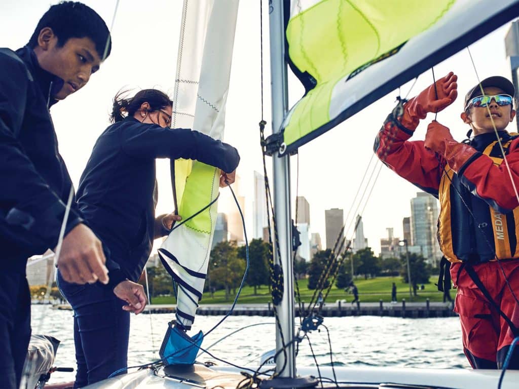 Three kids rigging up boat sailing.