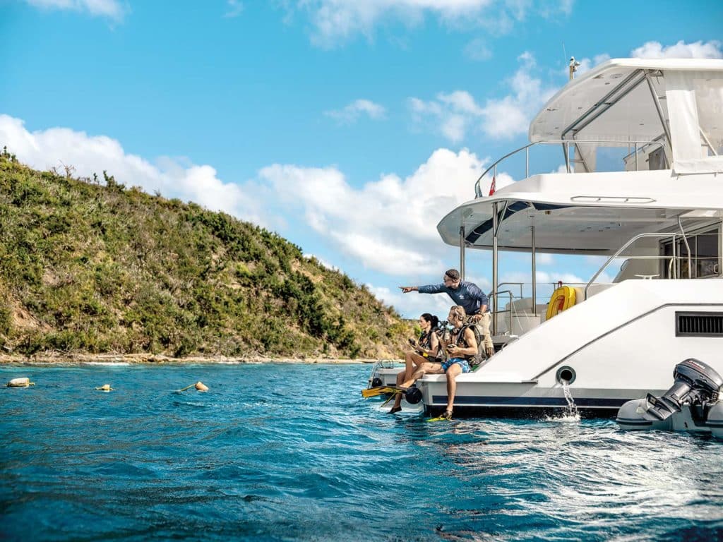 A couple puts on scuba gear on the back of a yacht.