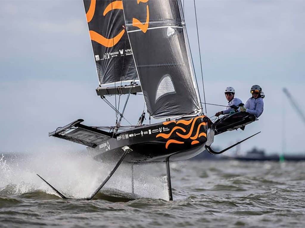 A team of two sailboat racers steer their fully-foiled sailboat across the water.
