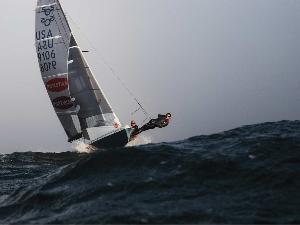 Two men sailing across rough waves.