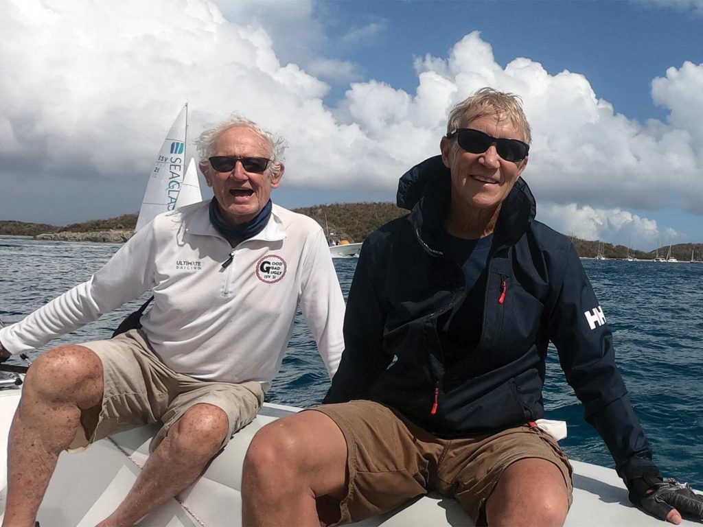 Two men sit on the deck of a sailing boat.