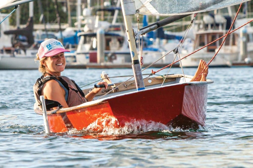 A woman pilots a sailboat dinghy.