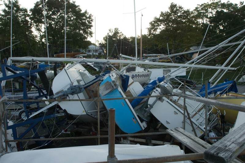 A row of keelboats blew over like dominos. The mast of a J24 that was knocked off its trailer is bent over top of the row of boats.