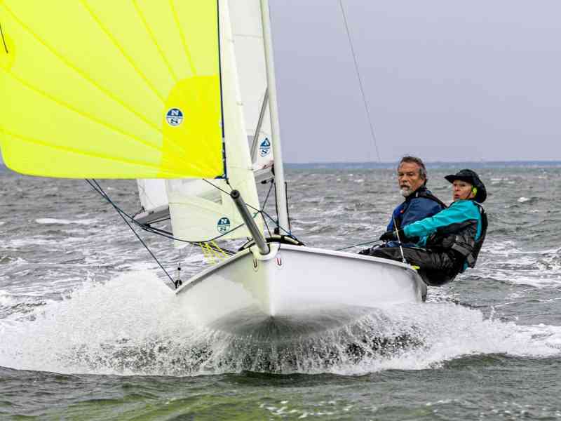 Two people pilot a sailboat across the water.