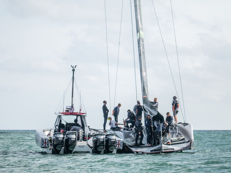 The crew of INEOS Britannia hoist the mainsail of their AC75, feeding the individual skins as the sails are hoisted and connecting internal systems as it goes aloft.